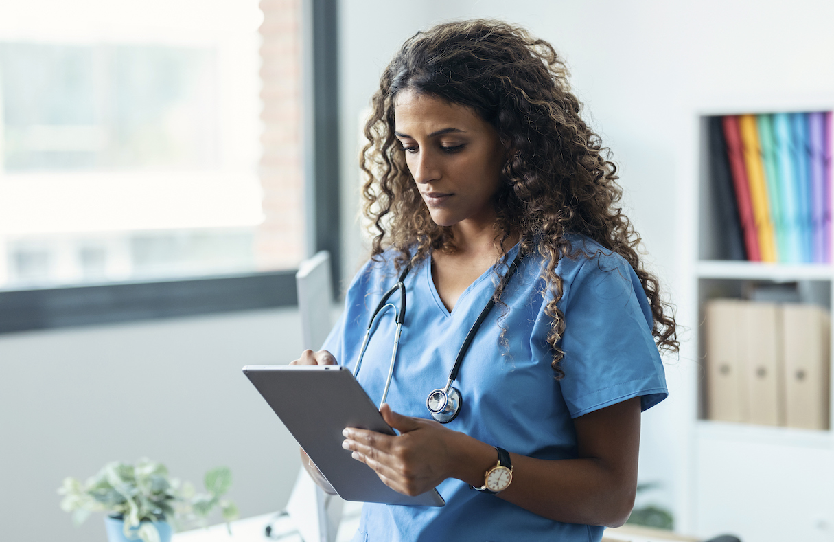 Female nurse using her digital tablet while standing in the consultation.