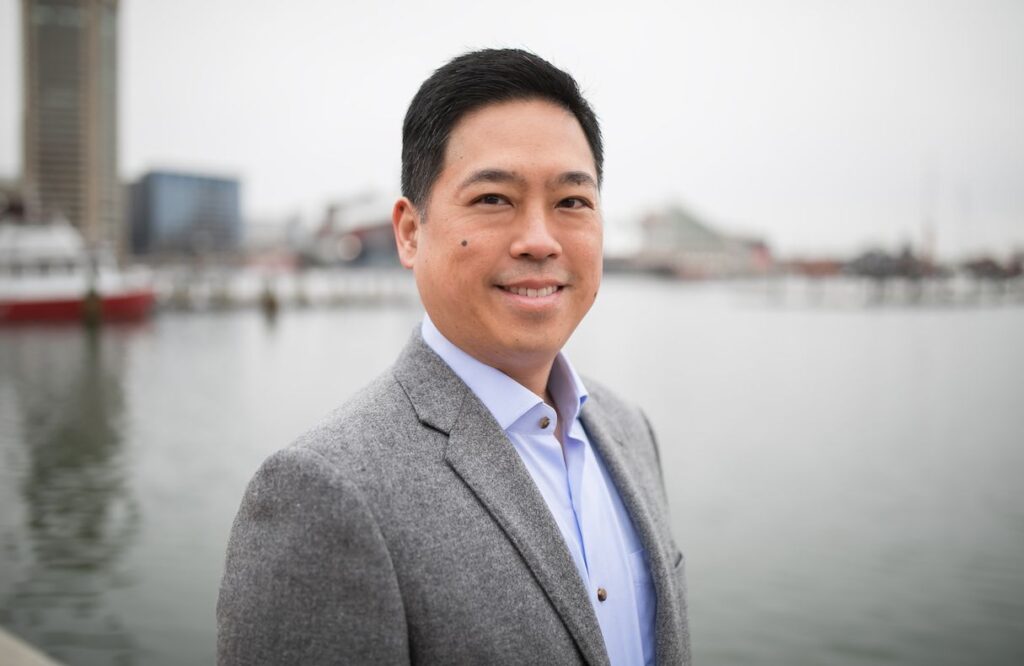 Headshot of man in grey sport coat at Baltimore's Inner Harbor