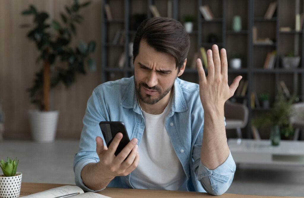 Man with short beard is annoyed while looking at cell phone