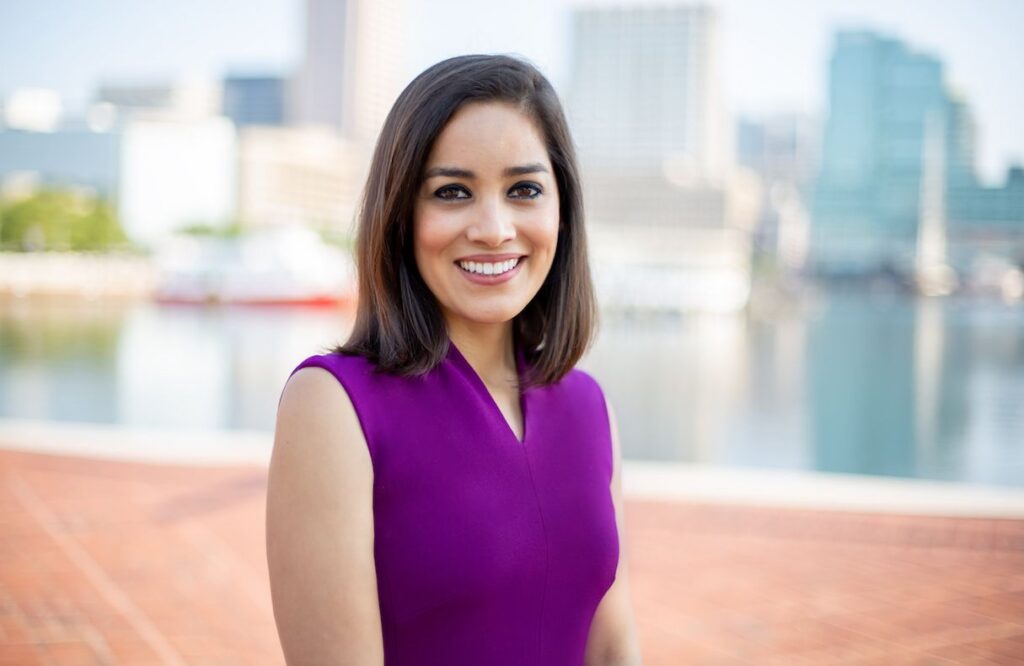 Woman with medium-length brown hair and purple dress smiles at the camera