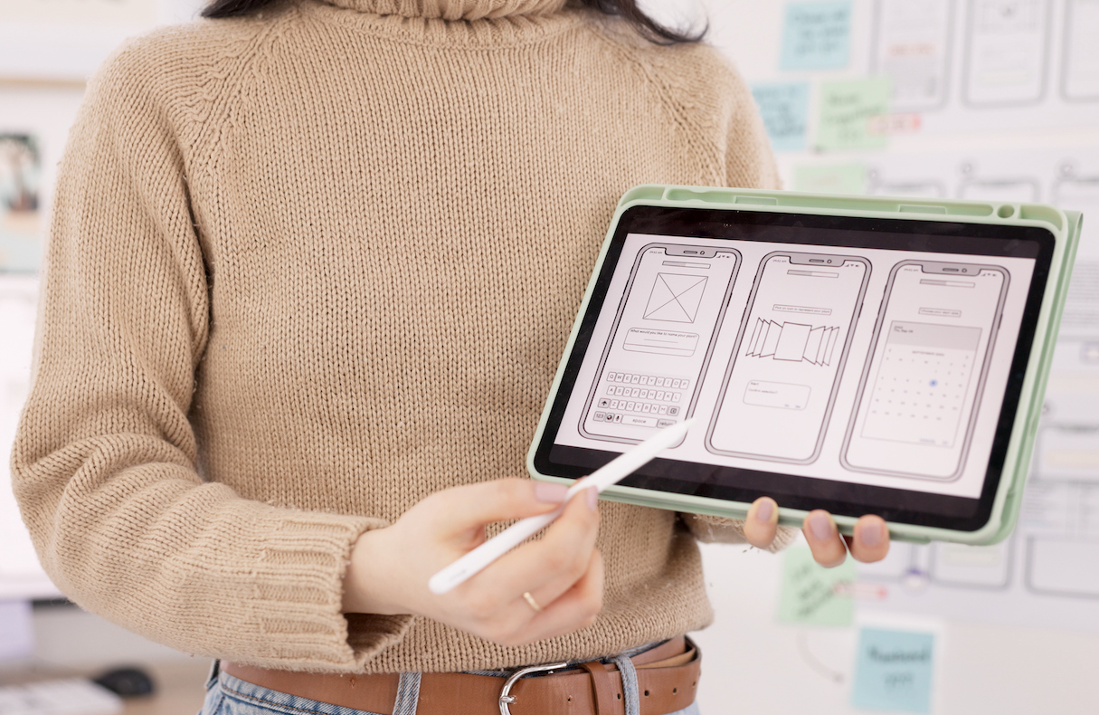 Woman pointing with a stylus at a tablet that has UX/UI images on the screen