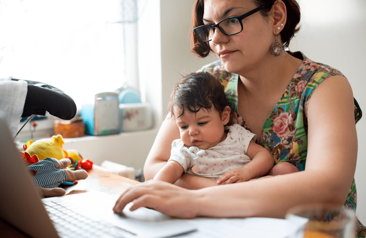 Woman holds a baby while trying to work from home