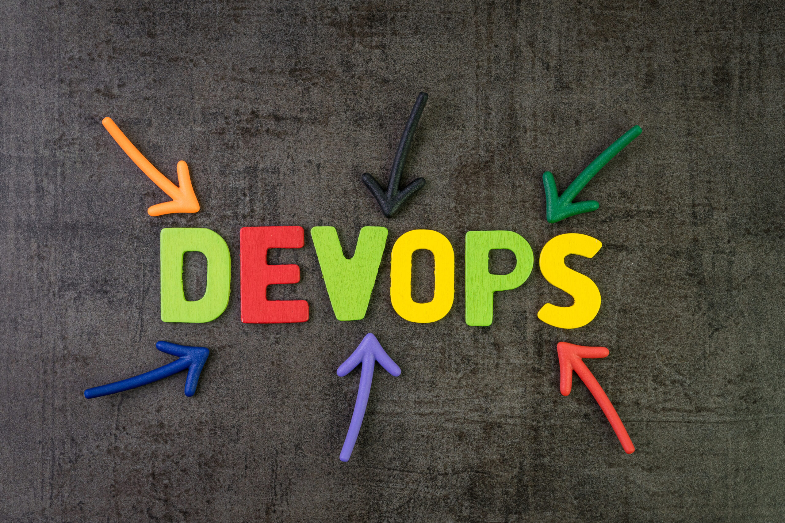 multi color arrows pointing to the word Devops at the center of black cement chalkboard wall.