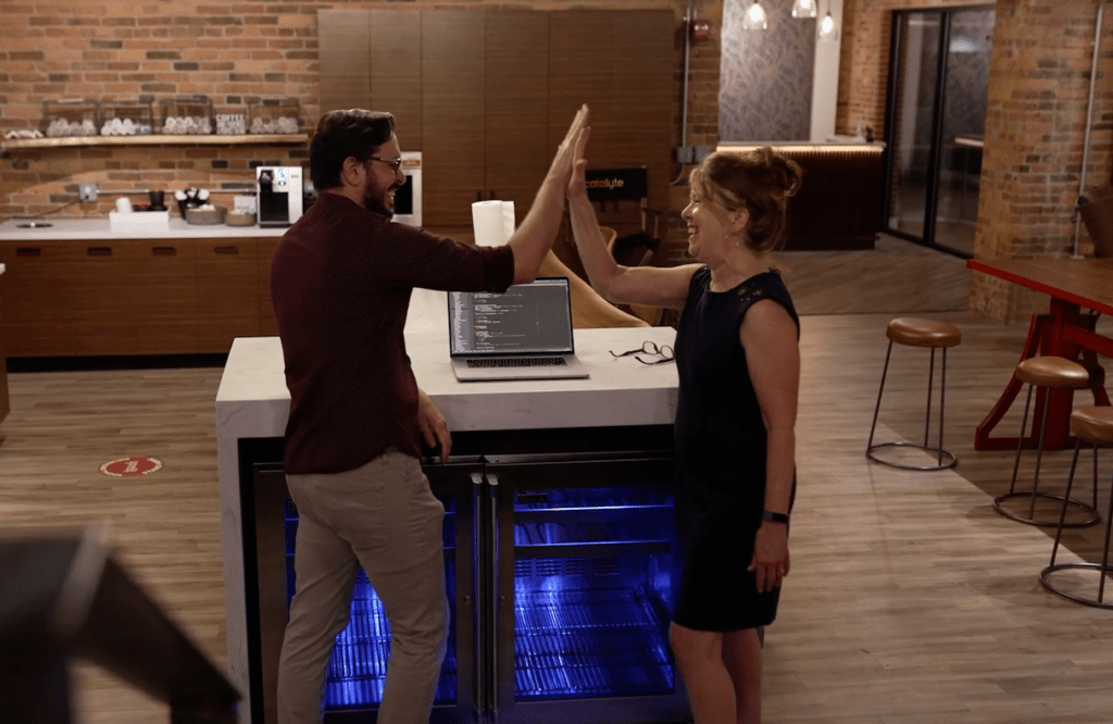 Man and woman high five each other in an office kitchen