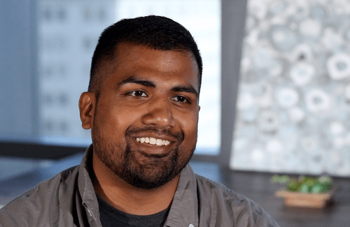 Man with dark, short hair smiles while sitting for a video interview