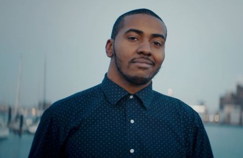 Man with short hair and buttoned up blue shirt looks at camera