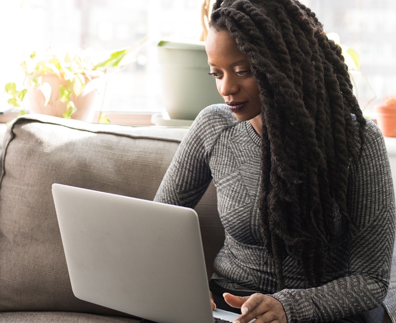 Woman with grey sweater sitting on a couch working on a laptop computer