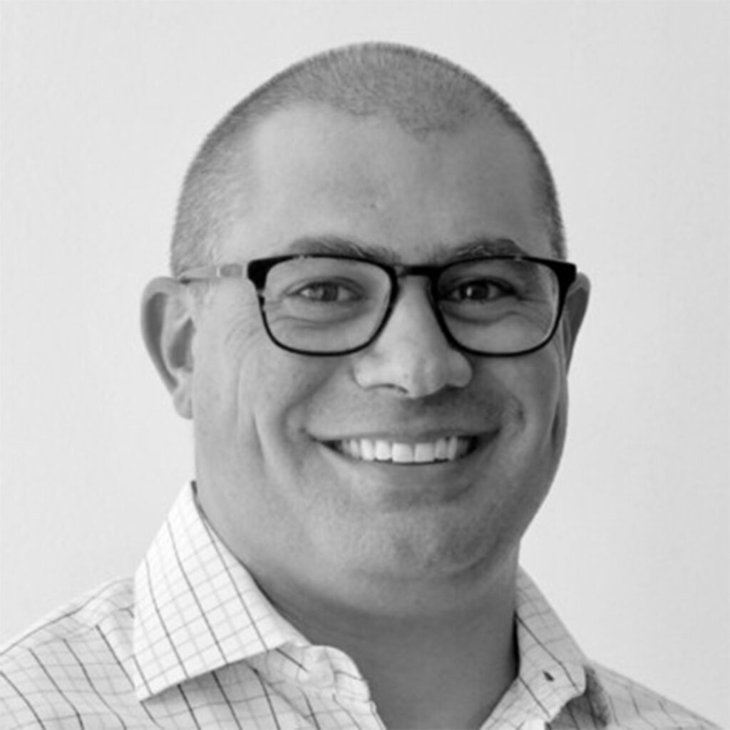 Man with buzz cut hair and glasses smiles at camera