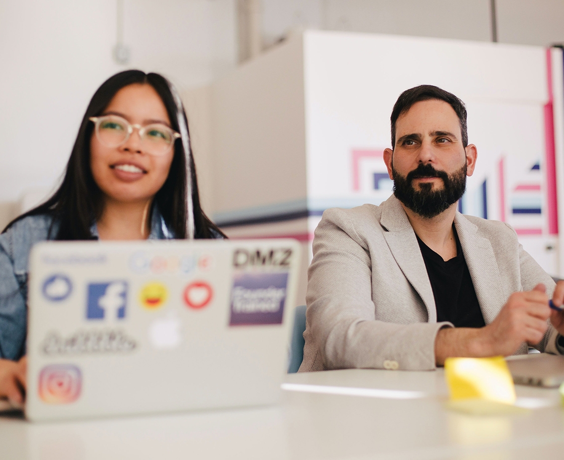 Women with glasses and man with beard shit at a table during a business meeting