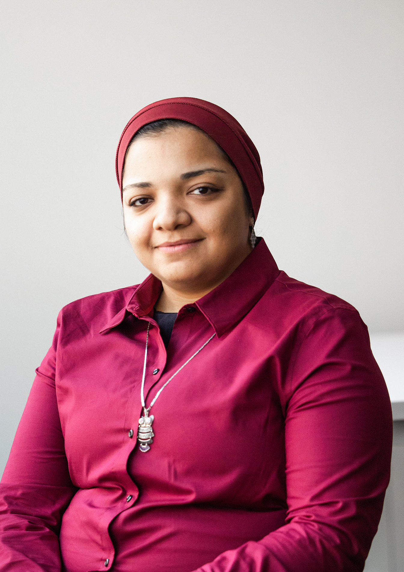 Woman with head covering and pink shirt sits smiling at camera