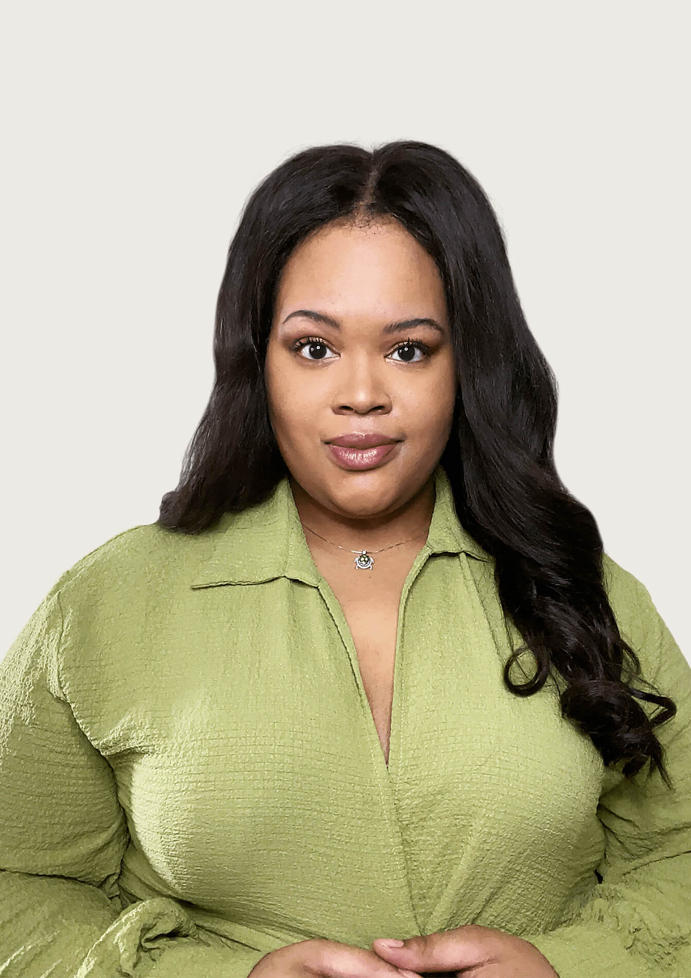 Woman with long black hair and a green shirt looks at the camera on a grey background