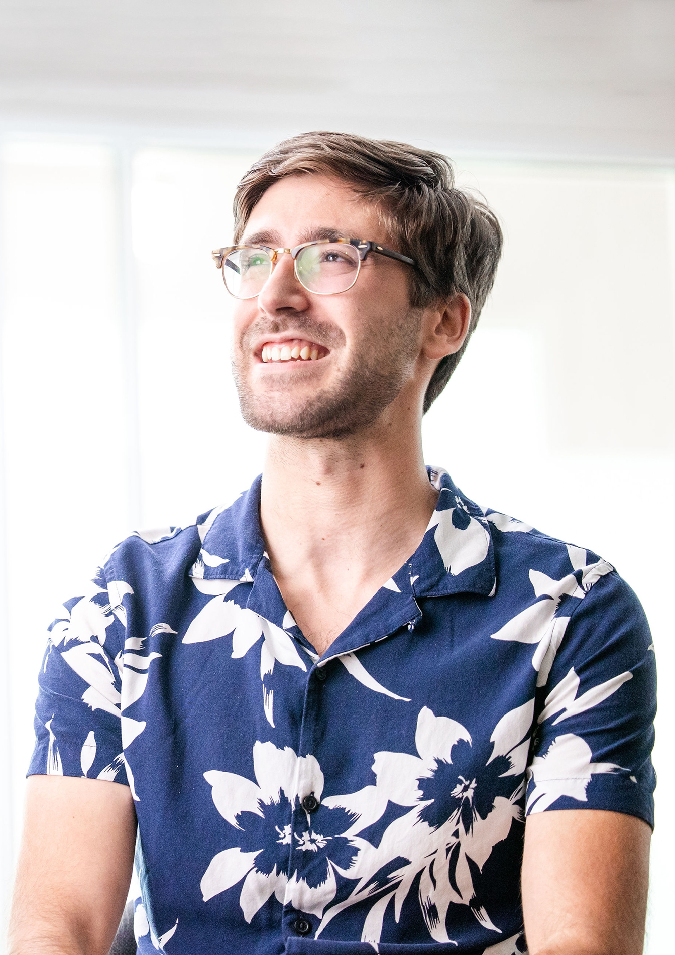 Man with glasses and blue floral pattern shirt looks off camera