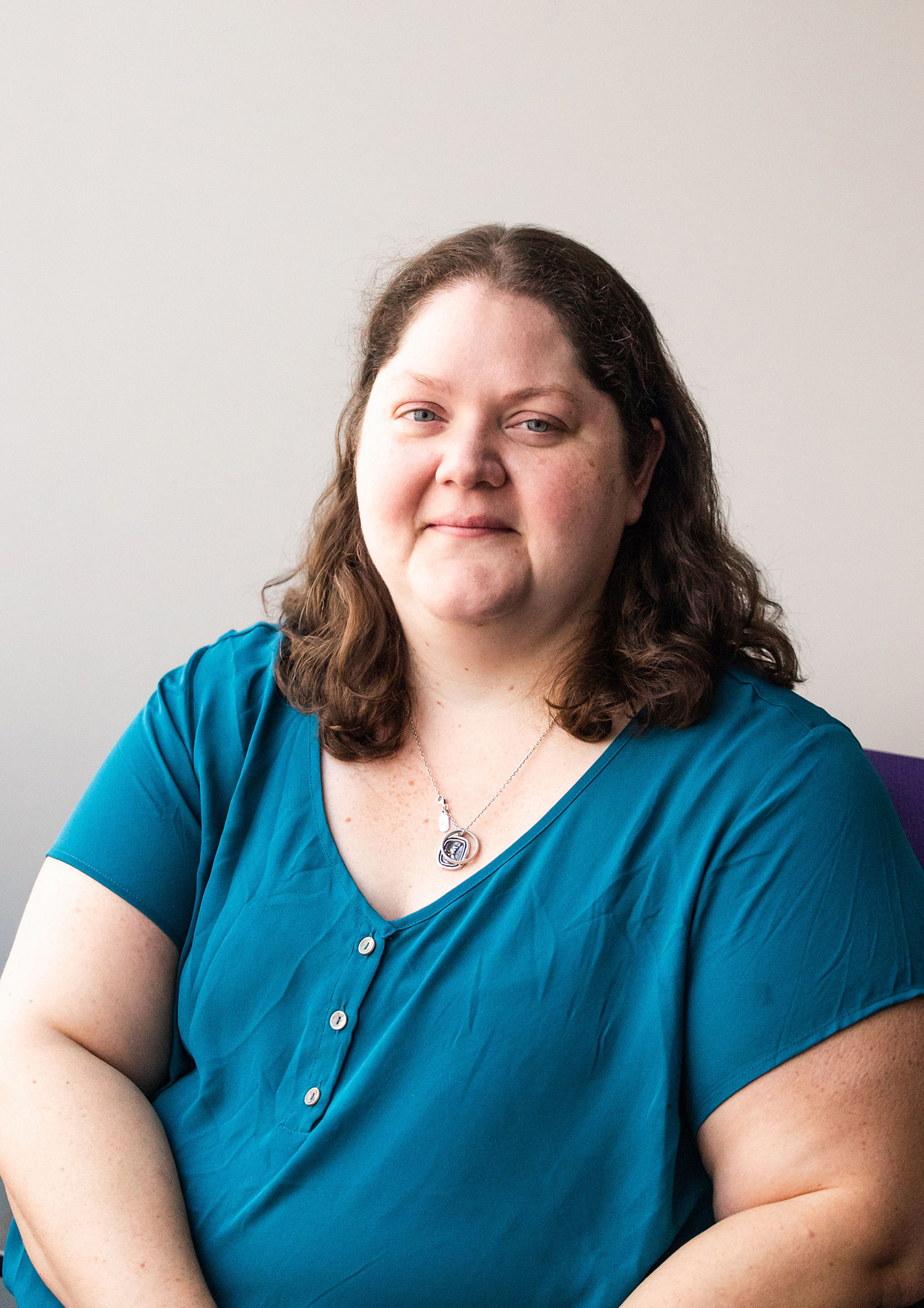 Women with long dark hair wearing a blue shirt sits in office chair smiling at camera