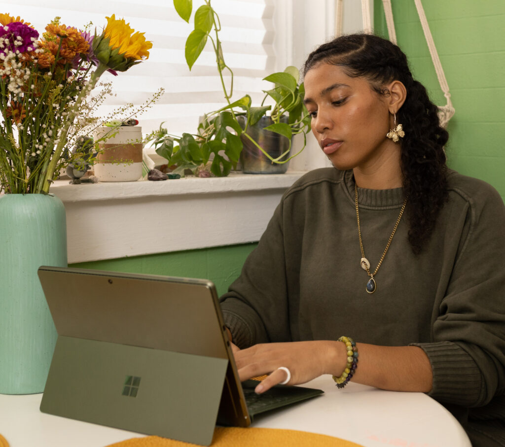 Woman with long black hair and green shirt works on a Microsoft tablet