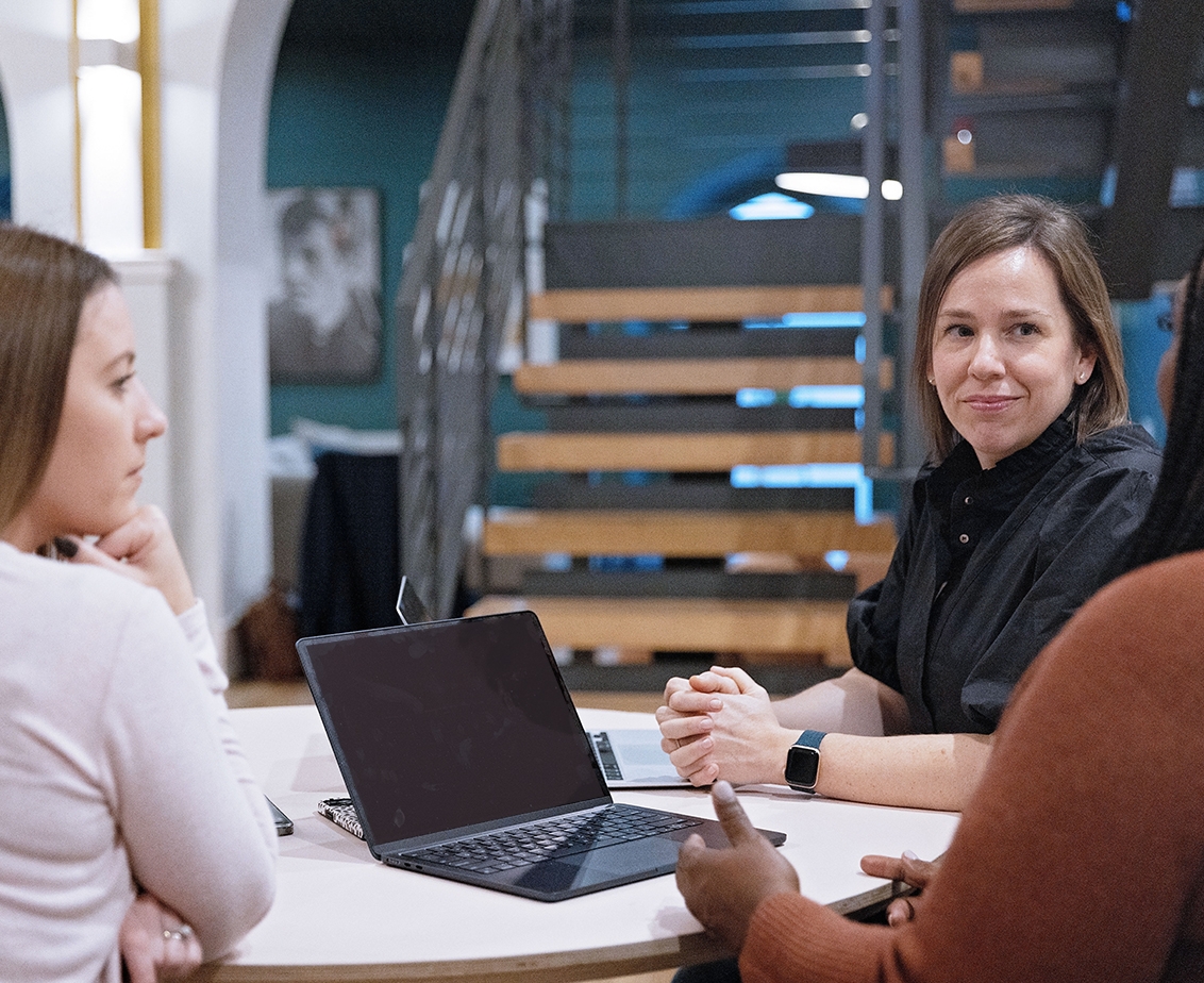 Three women sit around a table in an office having an informal meeting