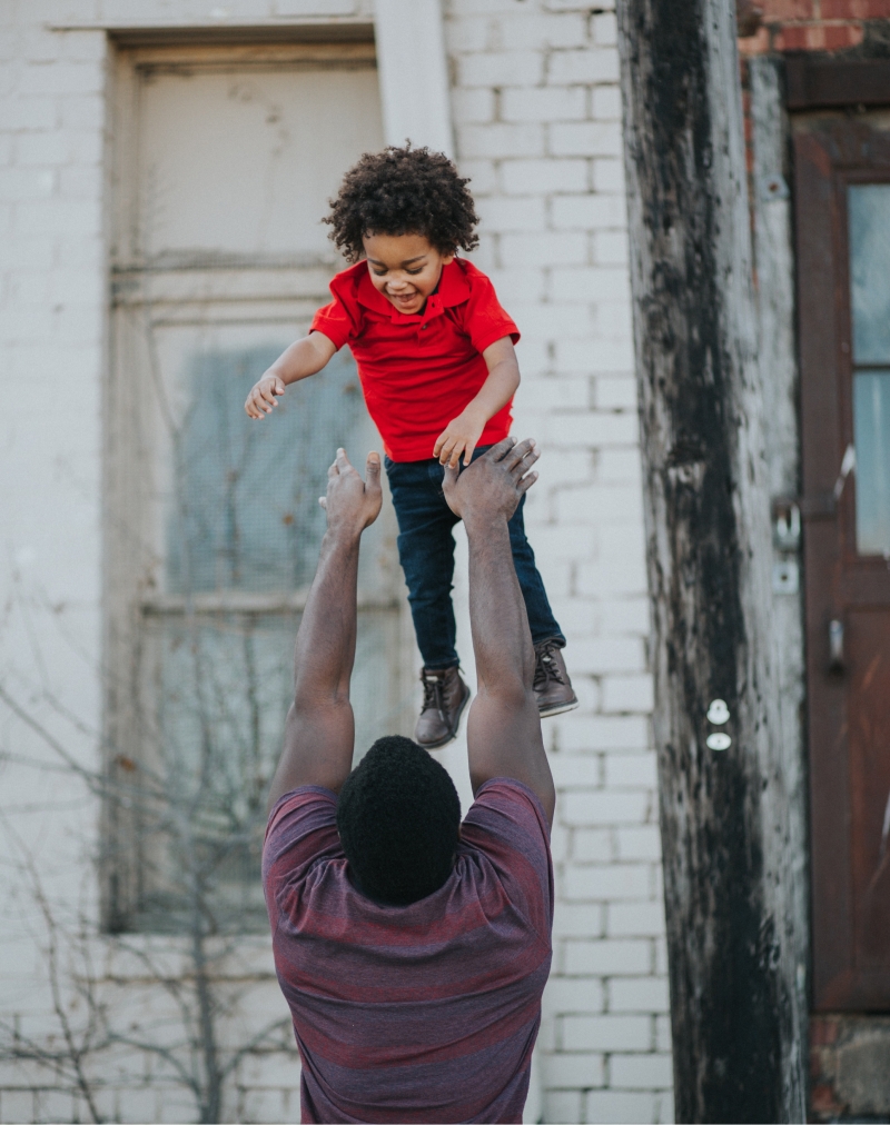 Man playfully tosses child wearing red shirt into the air