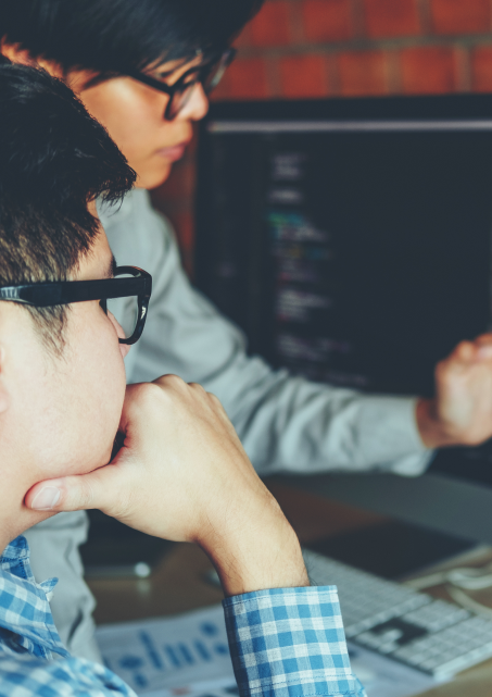 Two men in glasses look at code on a computer monitor.