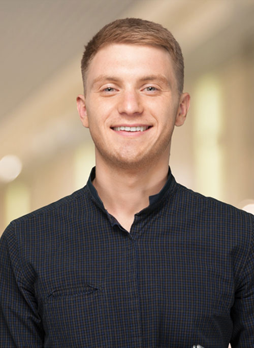 Short haired man with dark flannel shirt smiling at the camera