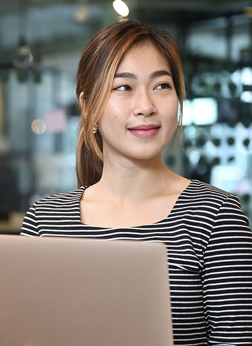 Woman with black and white striped shirt looks off camera with a laptop in front of her