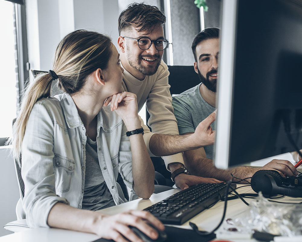 Three coworkers, two men one women, gather around a computer monitor