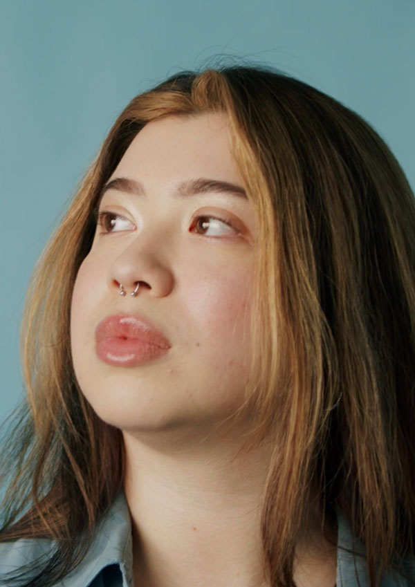 Woman with septum piercing looks just off camera against a blue background