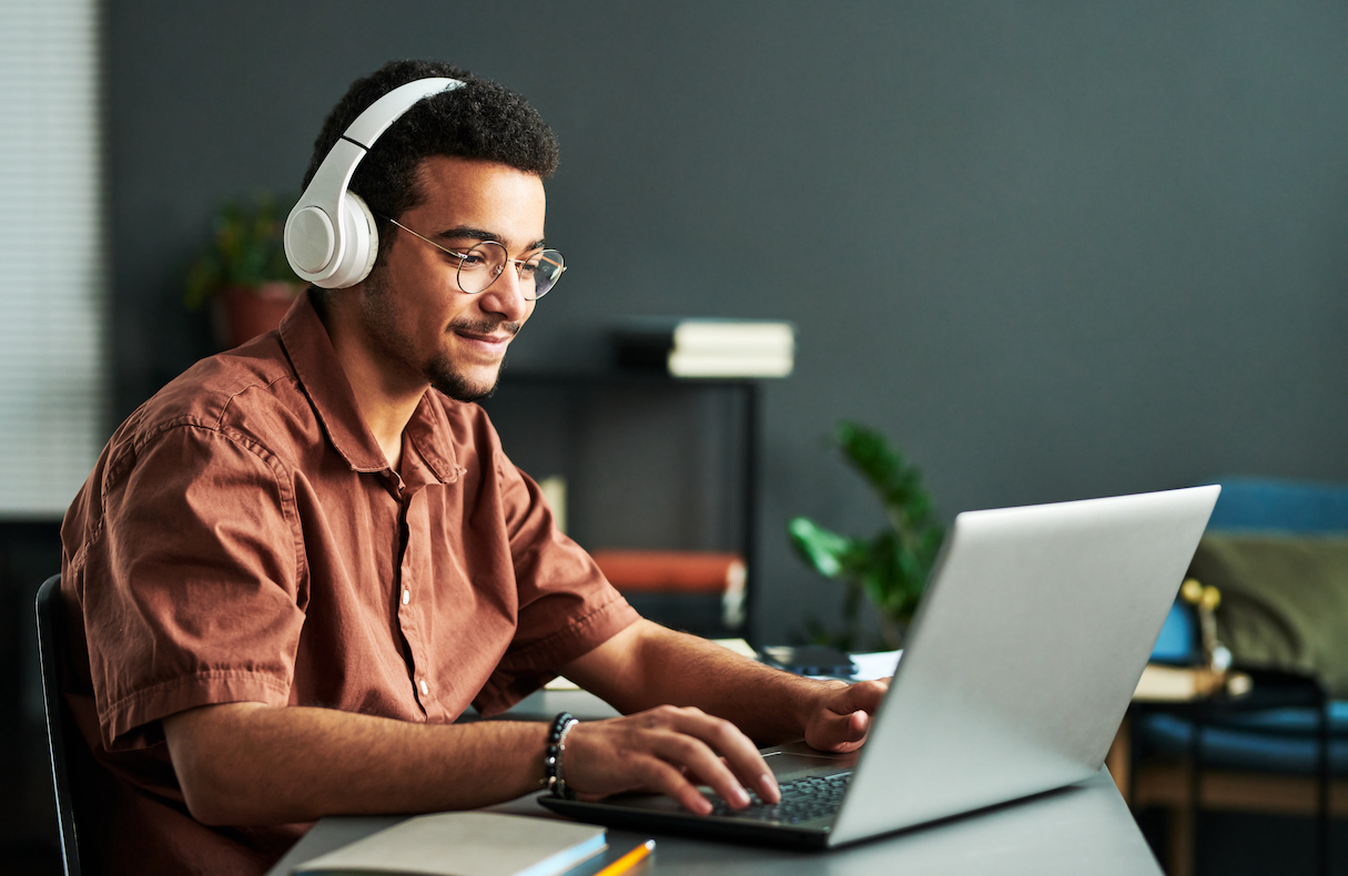 Young smiling man in headphones typing on laptop keyboard