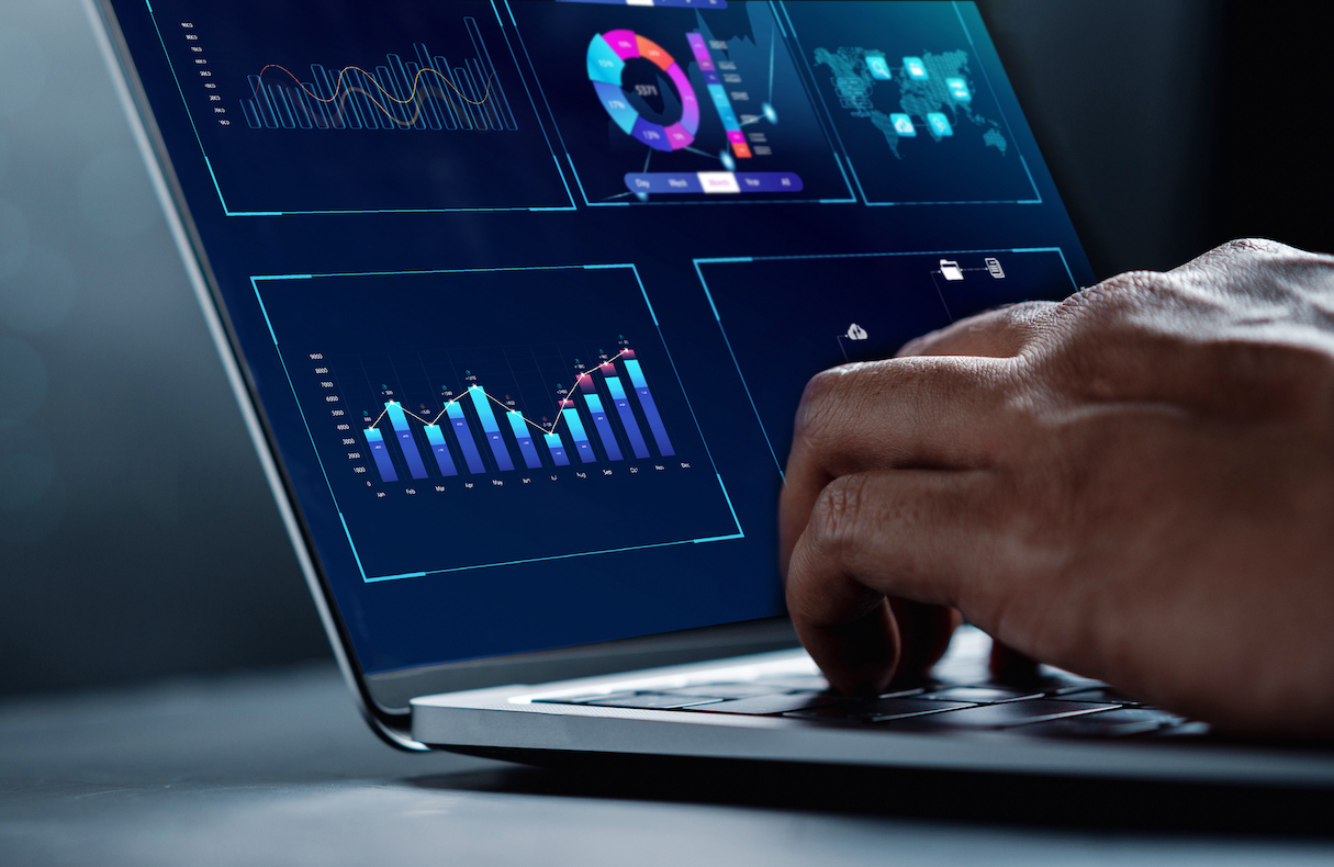 One hand typing on laptop keyboard with data charts and graphs on the screen